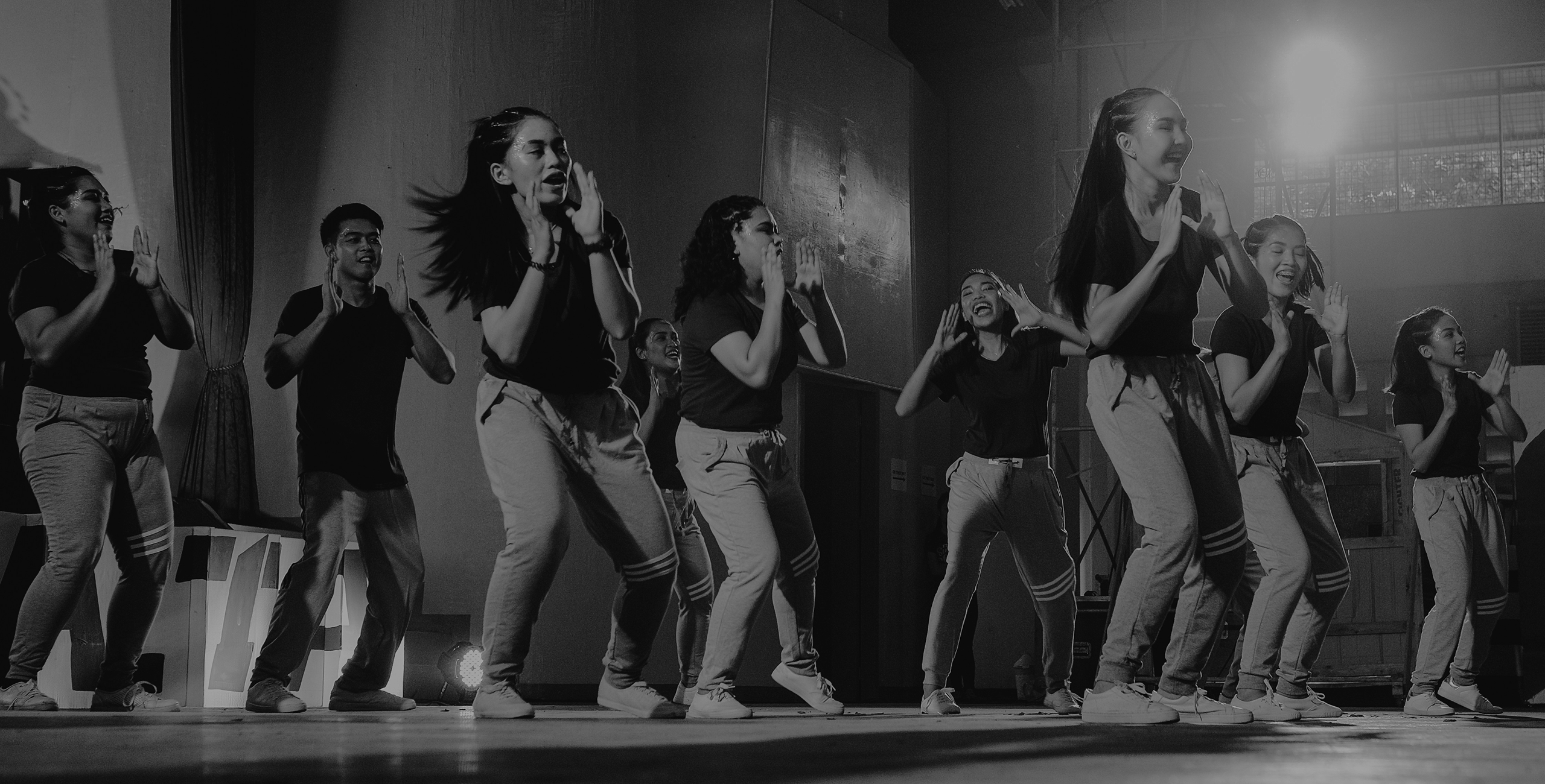 Black and white photo of teens rehearsing a dance routine on a stage.